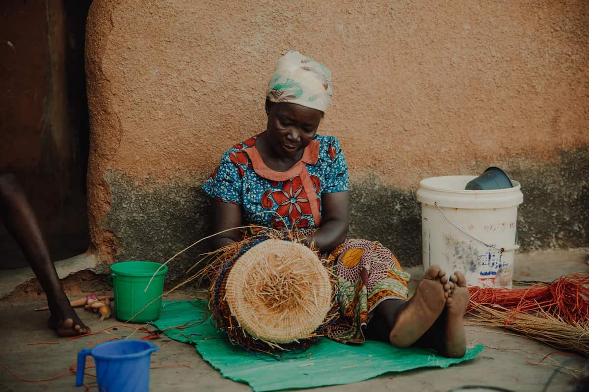 a view of a woman sitting on the ground and making a basket from the Veta Vera Grass