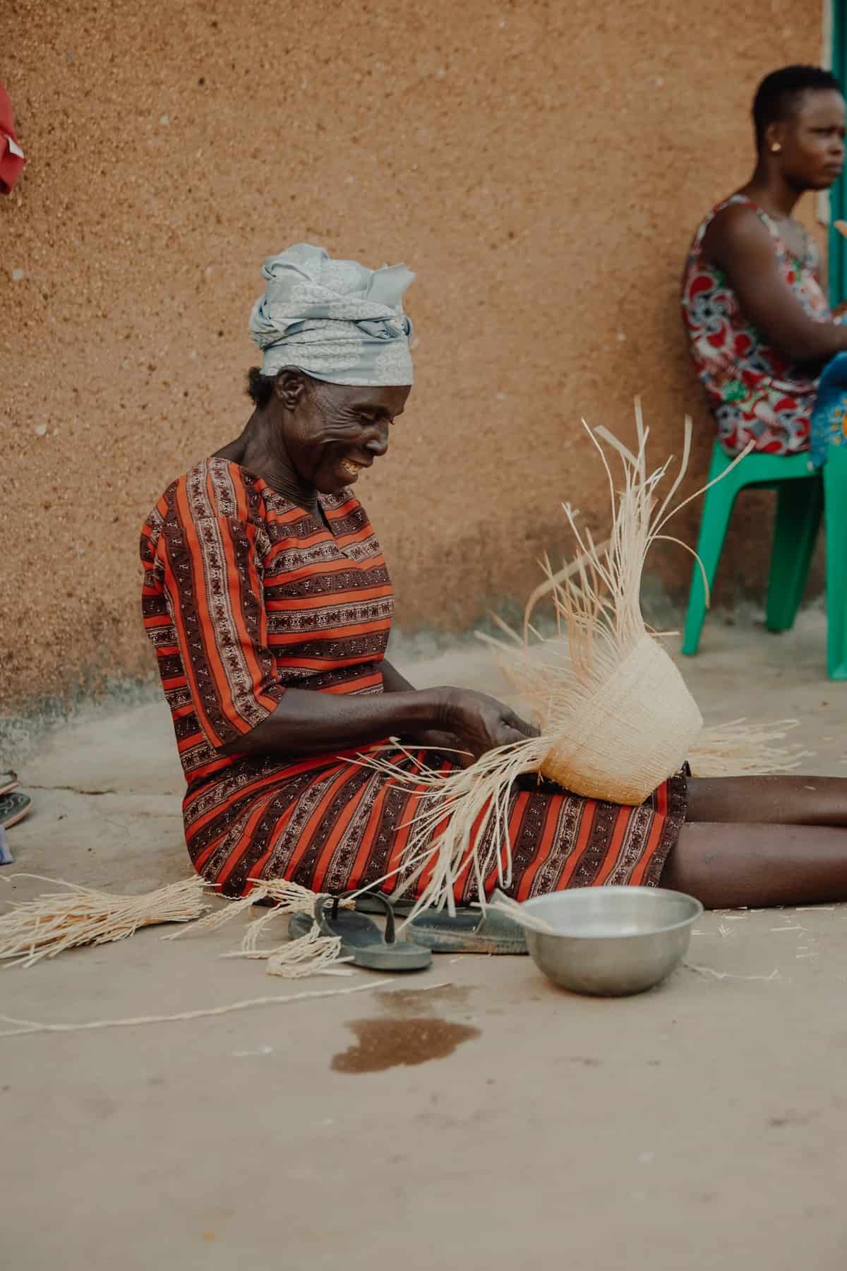Smiling woman from Ghana weaving Frafra baskets on her legs